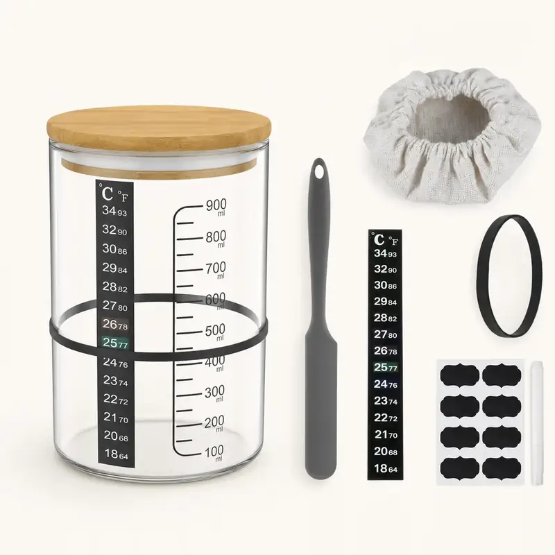 The 900 ml graduated fermentation jar with risen starter inside, cloth cover gathered over the rim and wooden lid beside it